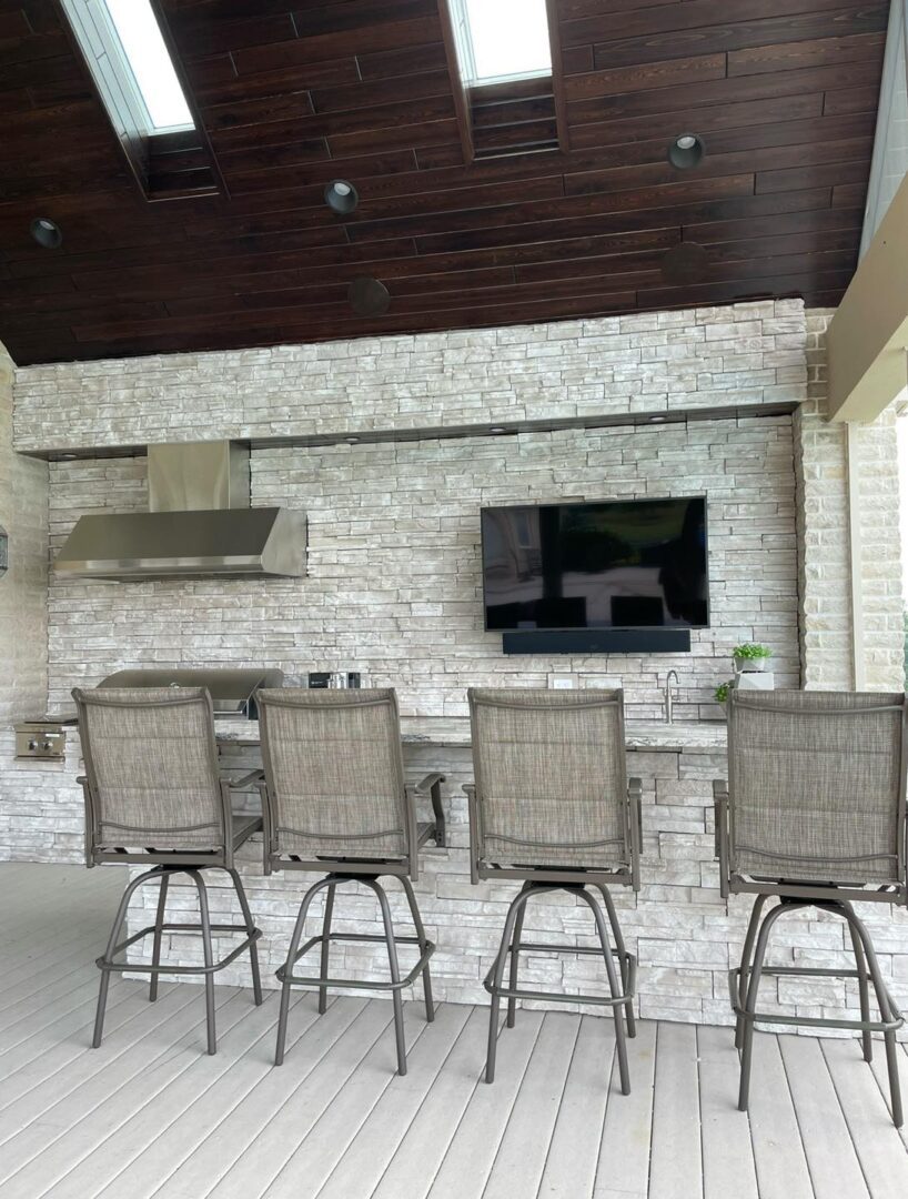 Outdoor kitchen with barstools and TV.