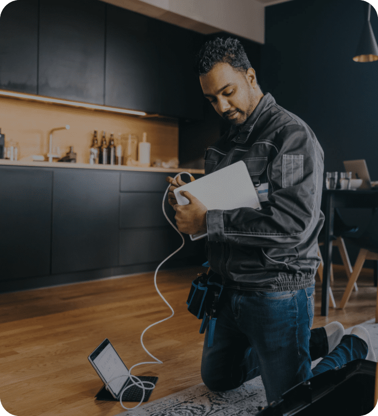 Man kneeling and assembling electronic equipment in a modern kitchen.