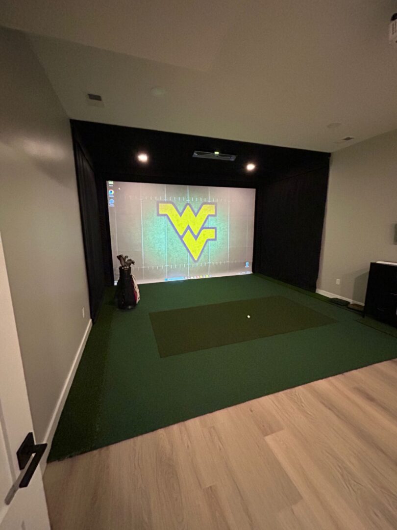 Indoor golf simulator setup with West Virginia University logo on the screen.