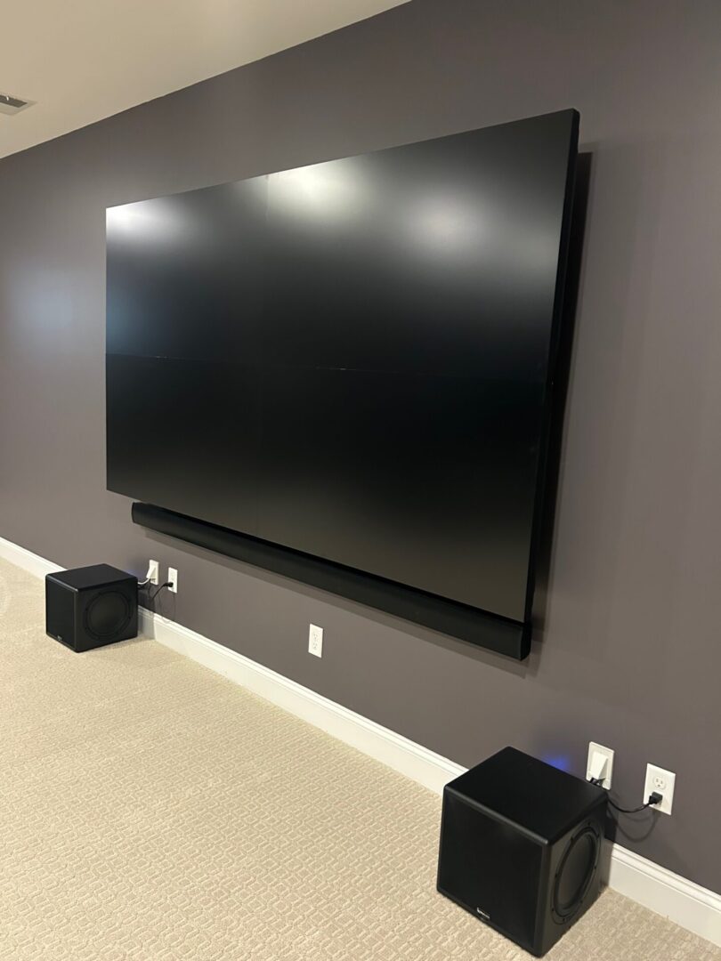 A modern flat-screen TV mounted on a gray wall with speakers below.