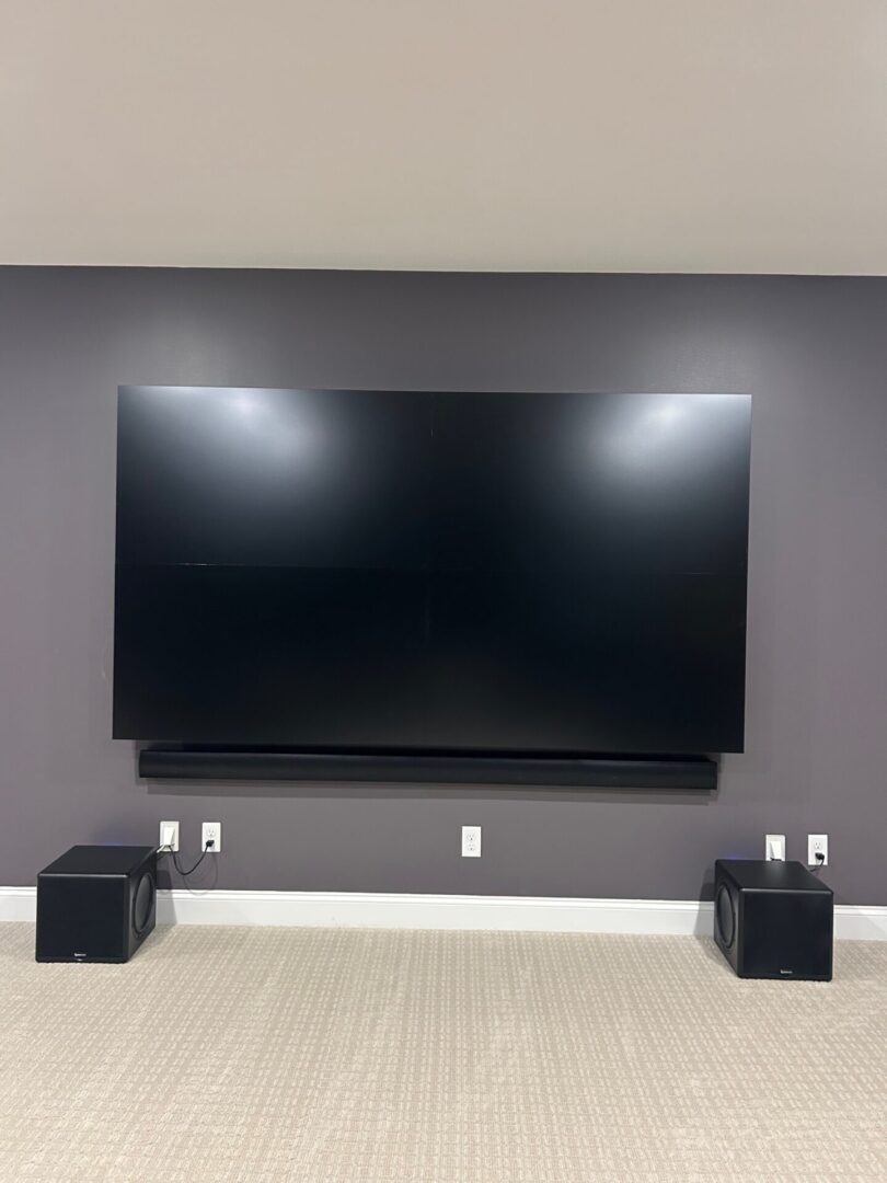 Large flat-screen TV mounted on a dark gray wall with two speakers below.