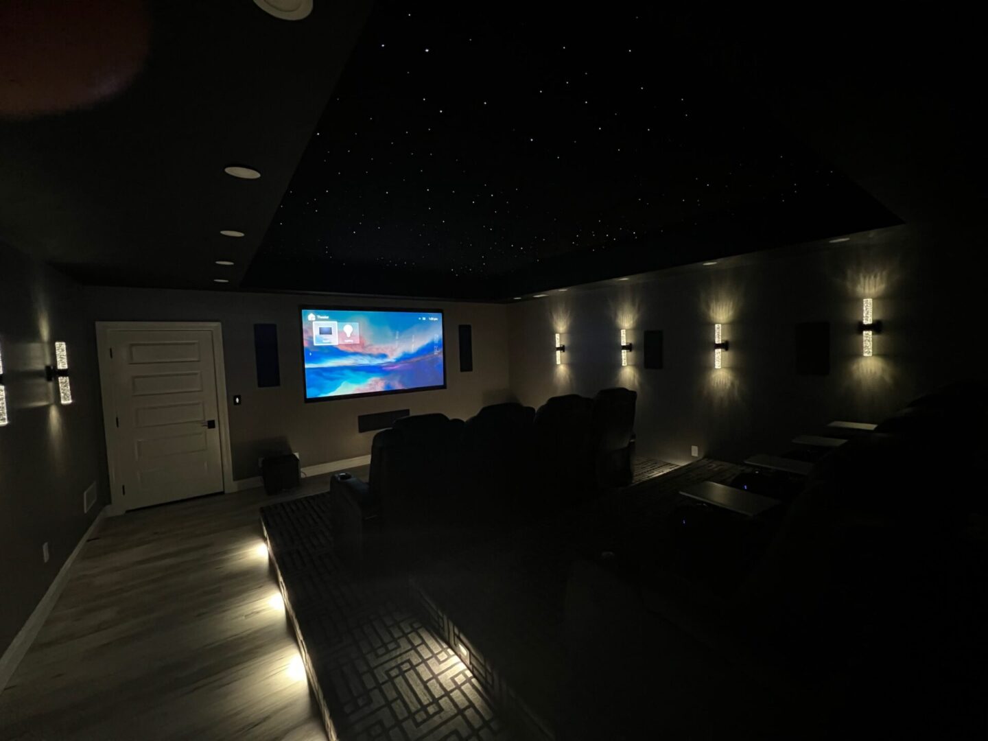 A cozy home theater with illuminated floor lights and a movie playing on the screen.
