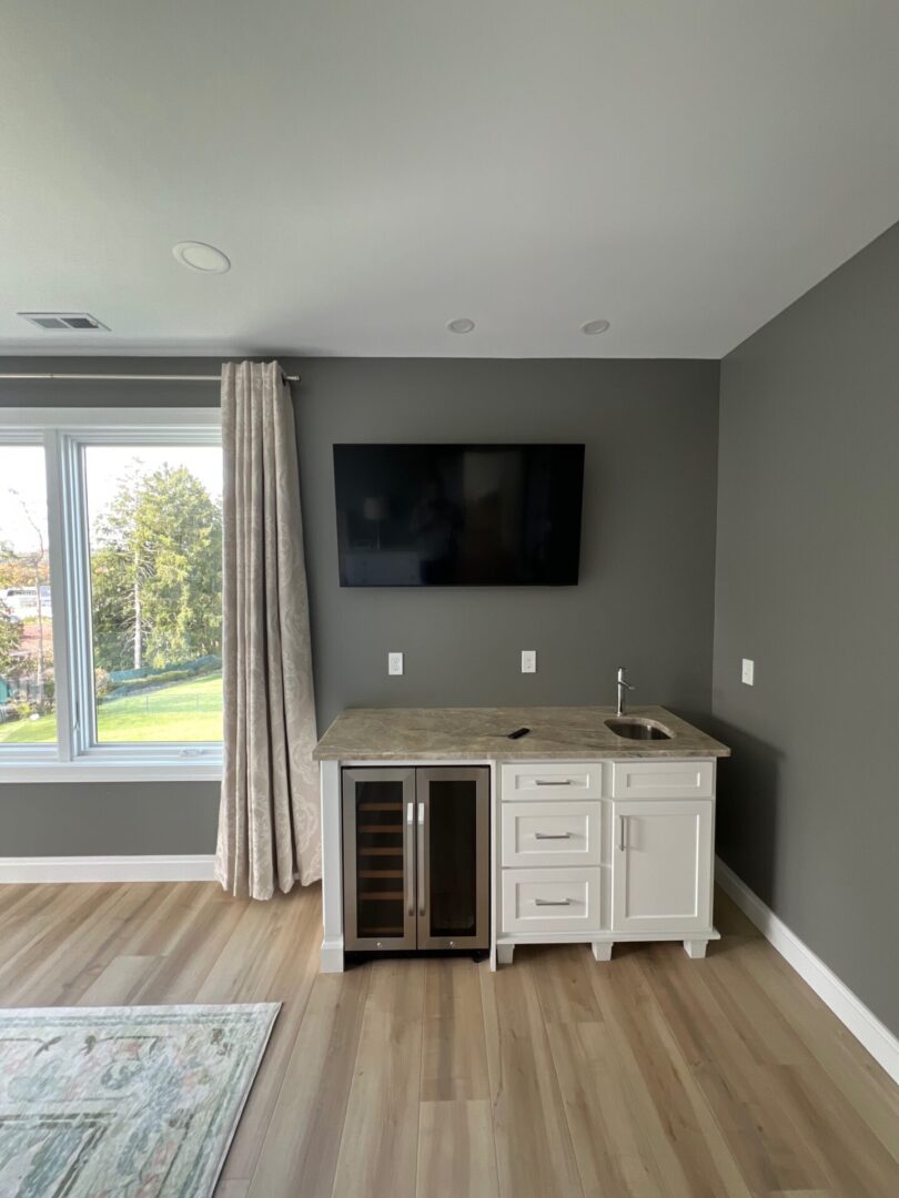 A modern kitchenette area with a wine fridge, sink, and mounted TV.