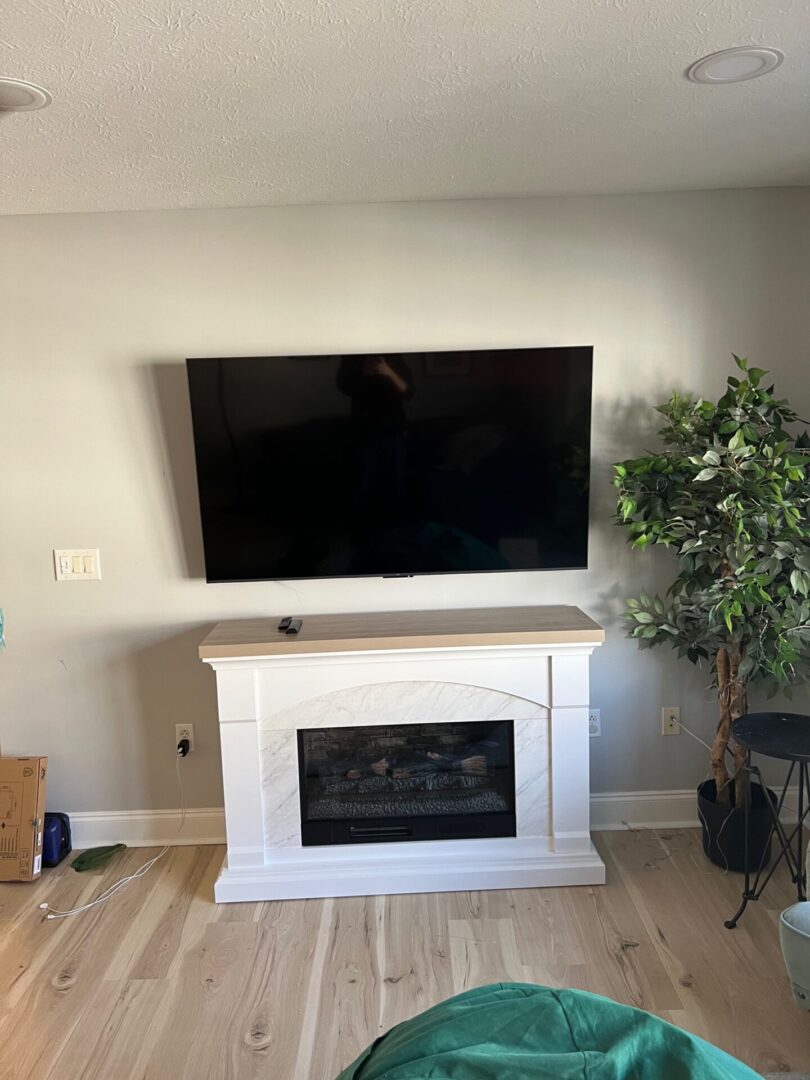 Modern living room with a wall-mounted TV above a white fireplace and a potted plant.